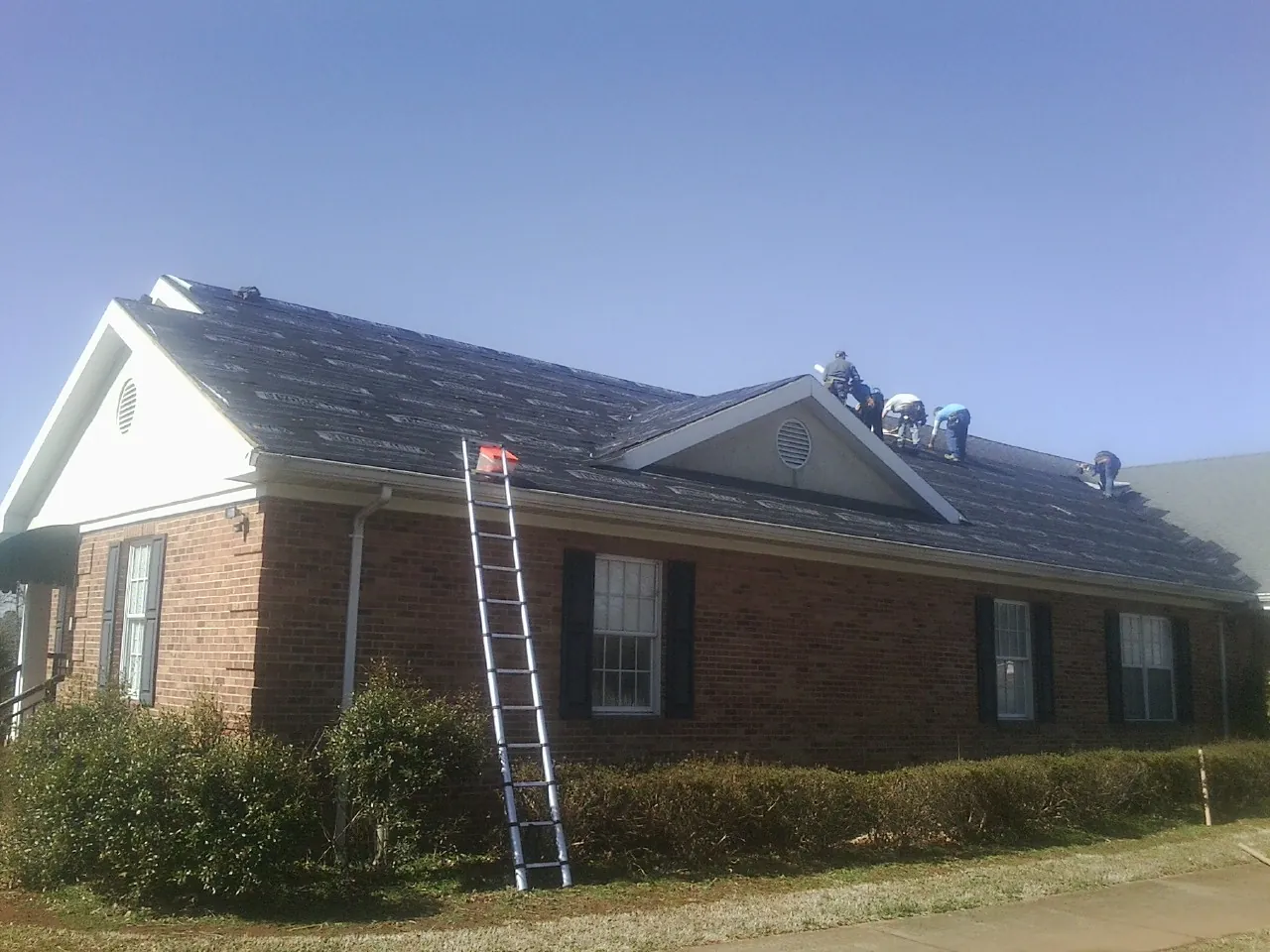 Crew tearing shingles off a brick ranch roof with a ladder set — Metal Roof Repair work by our crew in Valparaiso