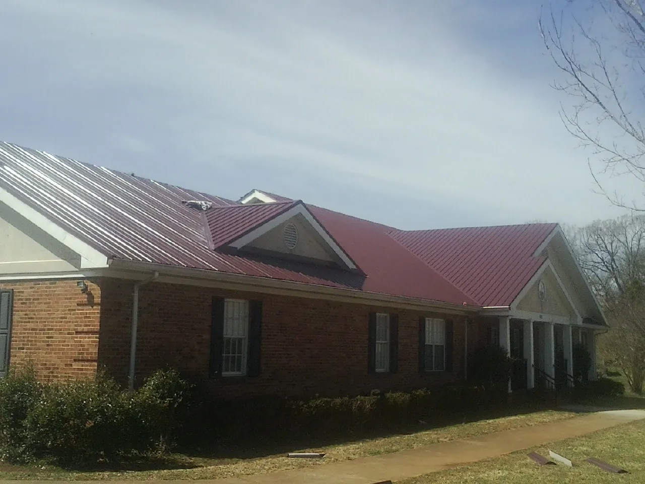 Red metal roof with gabled entries on a long brick building, from a Hail Damage Roof Repair job in Valparaiso