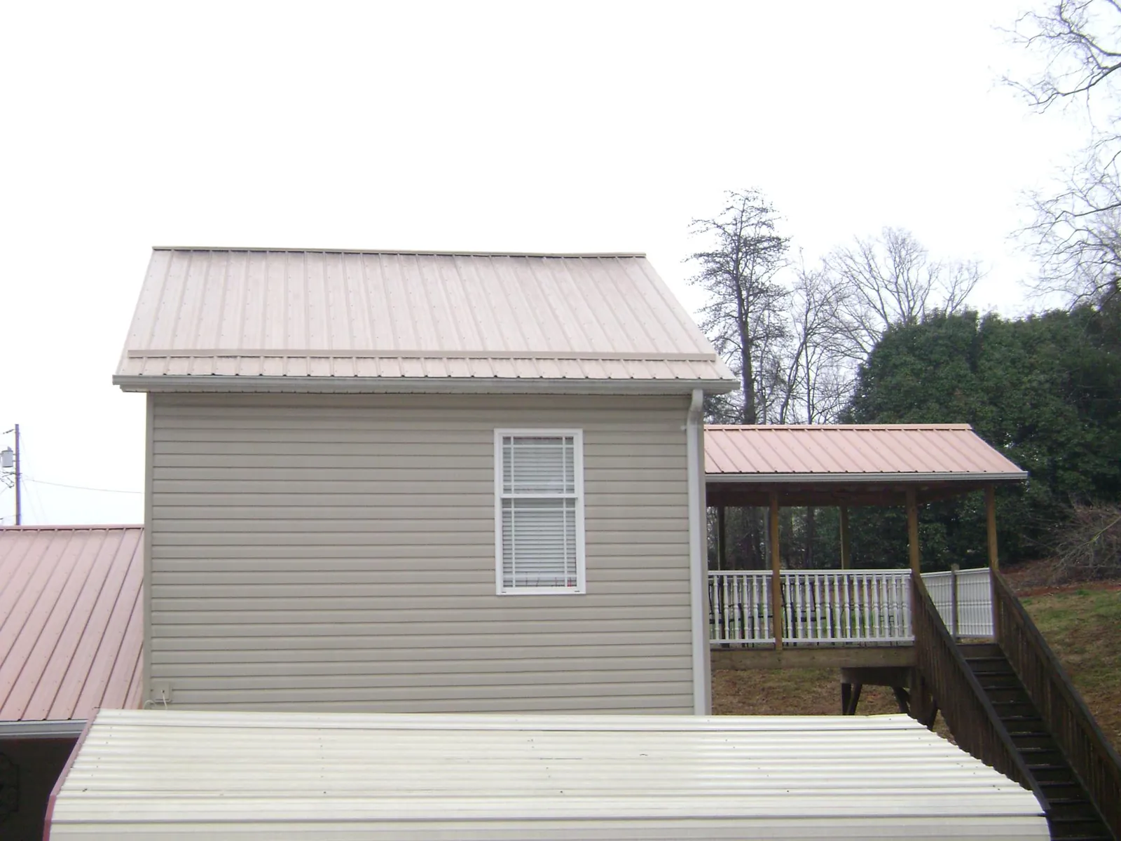 Tan metal roofs on a two story addition and attached porch, from a Roof Replacement job in Valparaiso